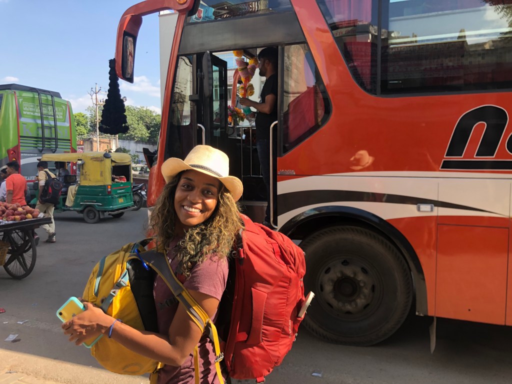 Amanda poses in a cowboy hat with her bags on her back in front of the Sleeper bus.