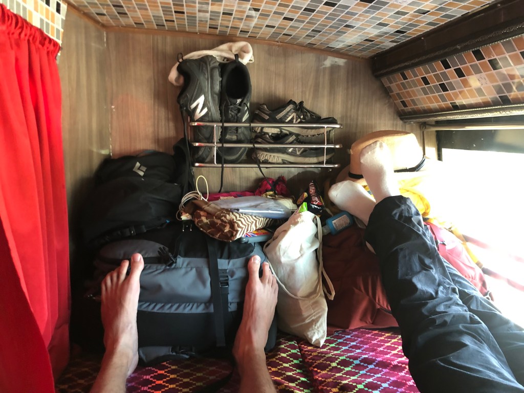 Adam and Amanda's feet are propped up on their stuff while in their sleeper bus compartment.