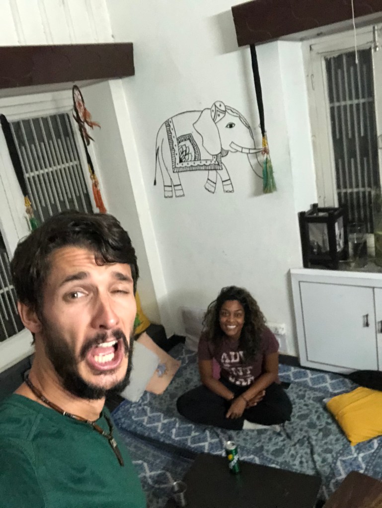 Adam and Amanda make tired faces in a selfie while in the main room of the hostel. Amanda is seated on the floor pillows.
